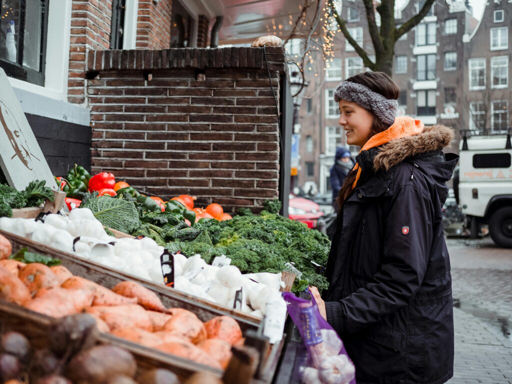 A young woman shops for fresh vegetables at an outdoor urban farmer's market in winter.