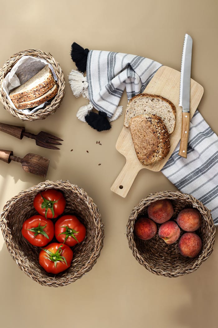 A cozy arrangement of sliced bread, tomatoes, and peaches with rustic wooden utensils on a warm surface.