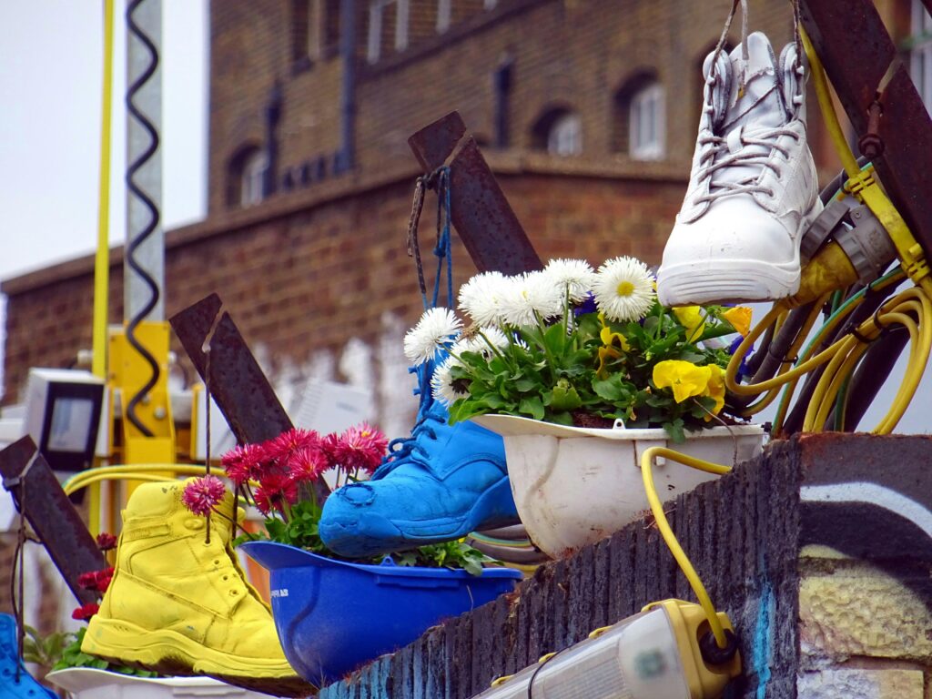 Unique urban display of vibrant flowers in colorful shoe planters on street wall.
