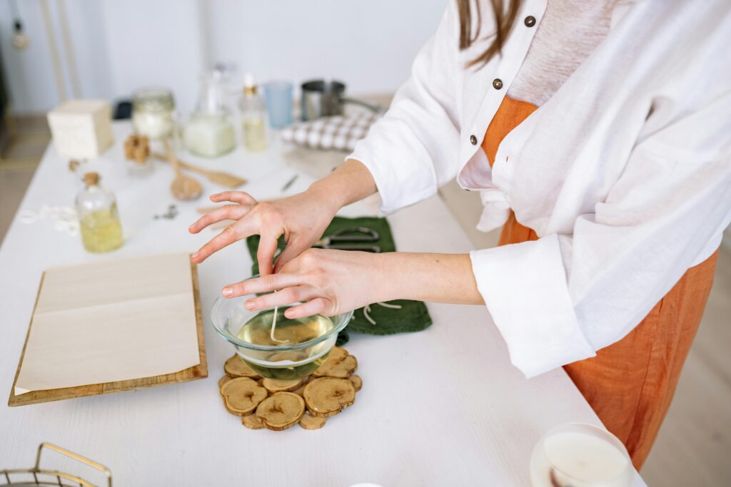 Hands crafting candles in a glass bowl during a DIY workshop with tools and materials.