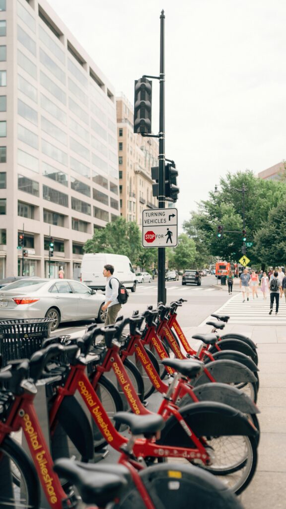 Red city bikes lined up on an urban street with people walking and cars passing by. Ideal for city life themes.