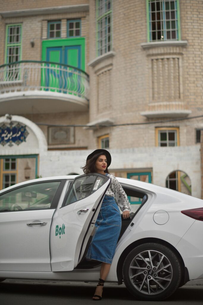 A fashionable woman steps out of a Bolt ride-share vehicle in an urban setting, showcasing modern city life.