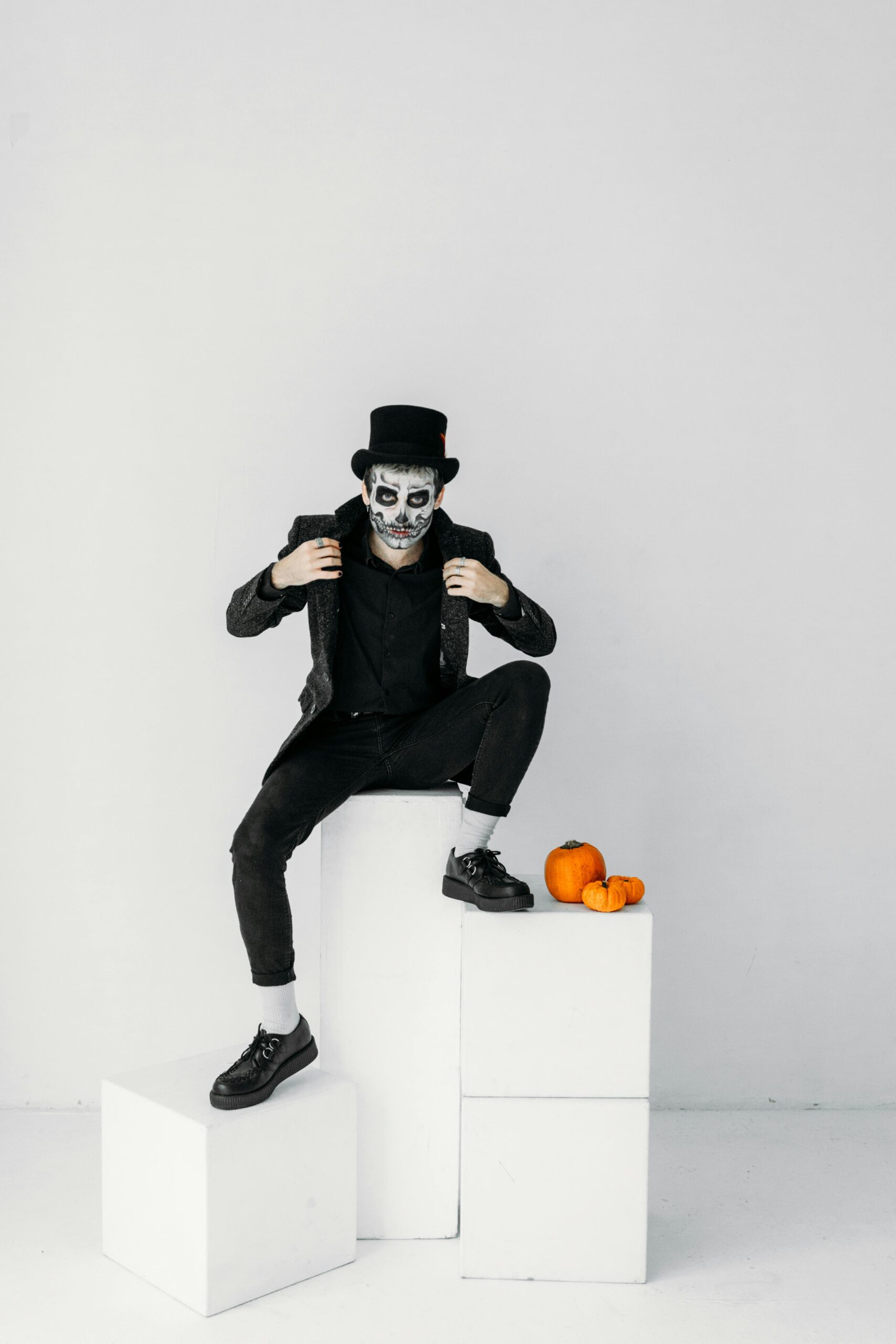 Man with skull makeup posing with pumpkins in a spooky Halloween setup.