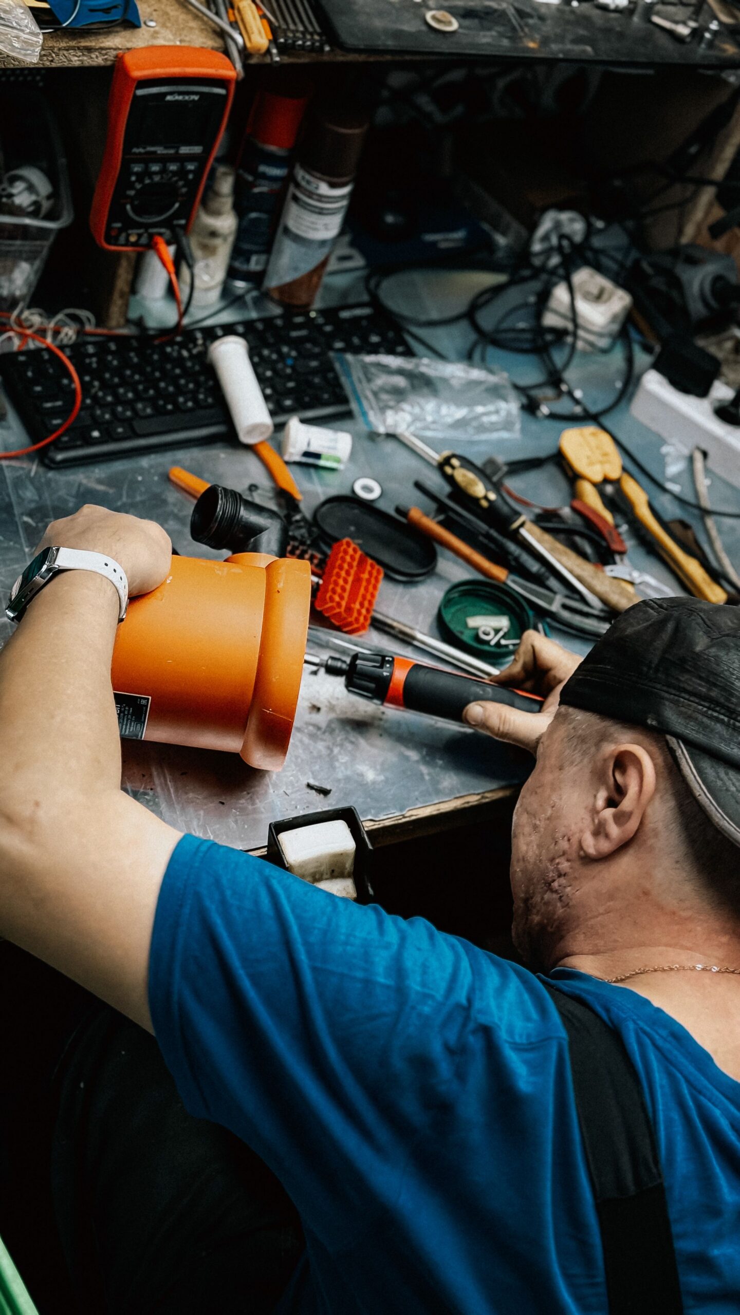 A technician repairing electronic equipment amidst various tools and gadgets in a messy workshop.